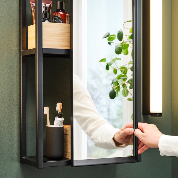 A bathroom with a wall-mounted ENHET mirror cabinet. Boxes with beauty products and a toothbrush holder sit on the shelves.