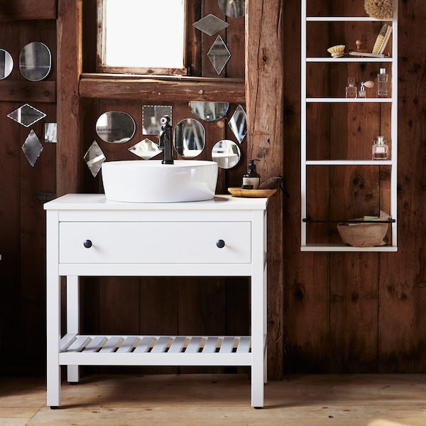 A bathroom with dark wooden walls, covered in small and oddly shaped mirrors and white HEMNES bathroom furniture.