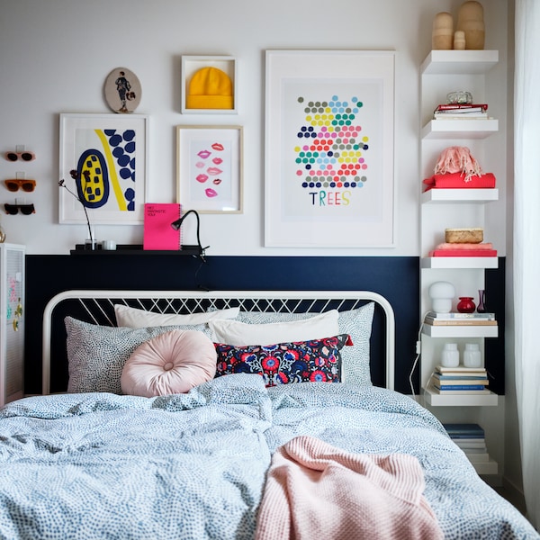 A bedroom in light shades and colourful decorations, a white NESTTUN bed made with blue-and-white TRÄDKRASSULA bed linen.