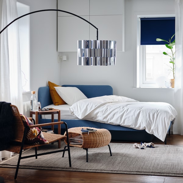 A bedroom with an upholstered bed frame with corner headboard, white quilt cover and pillowcase, a potted plant.