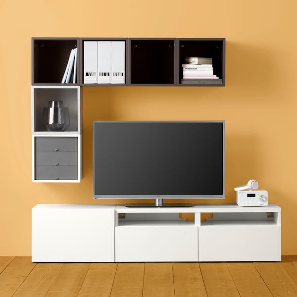 A BESTÅ/EKET cabinet combination for TV stands against an orange wall holding a TV and a lot of other objects.