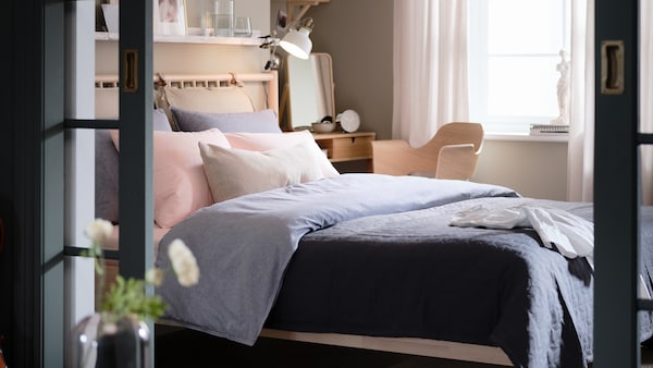 A birch BJÖRKSNÄS bed with a duvet in a dark blue KOPPARBLAD duvet cover stands in a bedroom near a window.