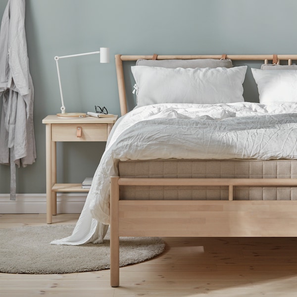A BJÖRKSNÄS bed frame with a mattress and white bedding on it stands in a bedroom next to a BJÖRKSNÄS bedside table.