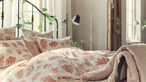 A black SAGSTUA bed with VITPYROLA bed linen, which has a pattern of seashells and coral, stands near a window in a bedroom.