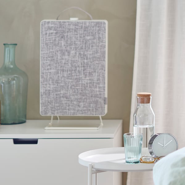 A chest of drawers with a FÖRNUFTIG air purifier and a vase on top stands next to a small table and a curtain.