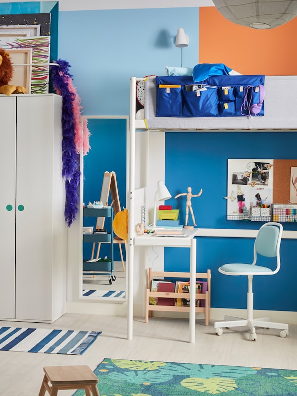 A children’s room with a white VITVAL loft bed with a built-in desk underneath, near a white wardrobe.