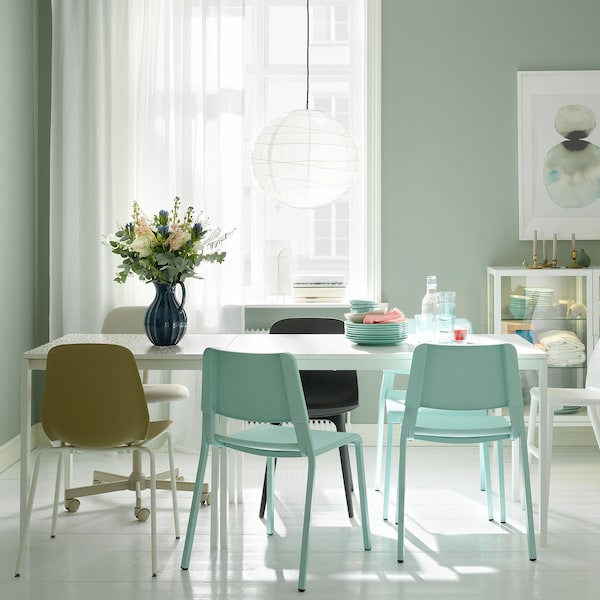 A dining area with two white MELLTORP tables, a white REGOLIT pendant lamp and assorted seating.