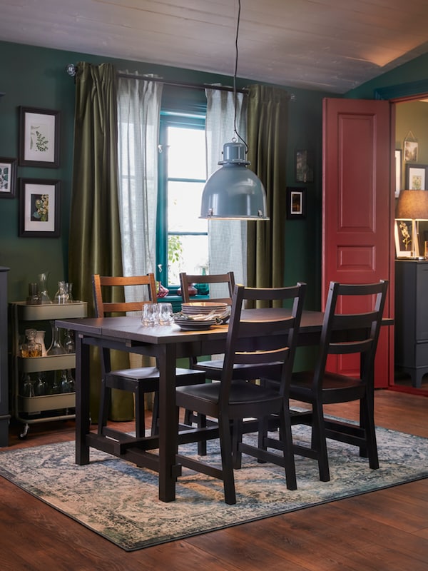 A dining room with a table and four chairs in black, an oriental-patterned rug and a grey-turquoise pendant lamp.