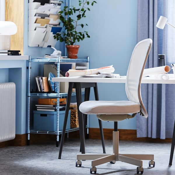 A FLINTAN office chair beside a white desk and an OMAR shelving unit filled with papers and file boxes in a blue office.