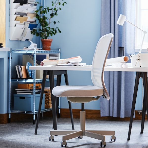 A FLINTAN office chair beside a white desk and an OMAR shelving unit filled with papers and file boxes in a blue office.