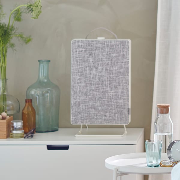 A FÖRNUFTIG air purifier on a white chest of drawers. There is a GLADOM tray table with a KORKEN bottle and glass next to it.