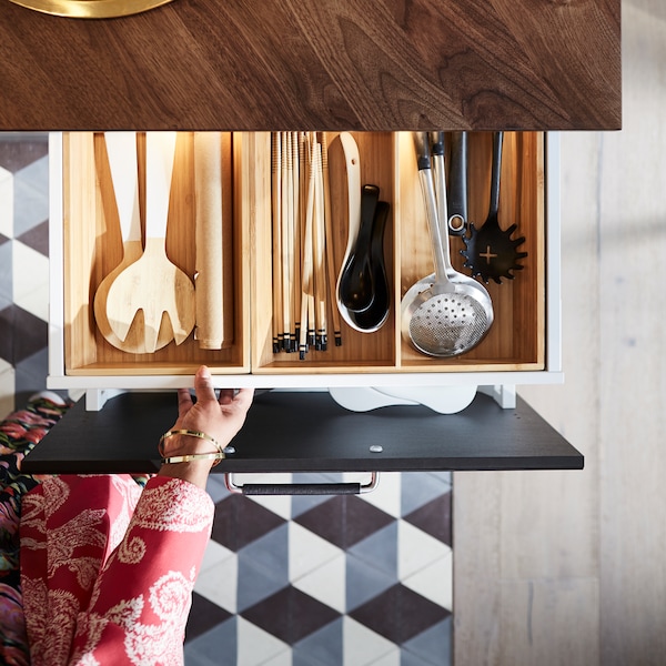 A hand pulling out a drawer below a dark wood countertop with wooden inserts filled with kitchen utensils.