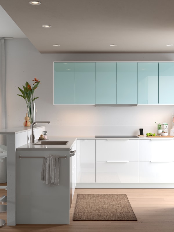 A large, bright open-plan kitchen with white and turquoise door fronts and a vase of flowers on the worktop above the sink.