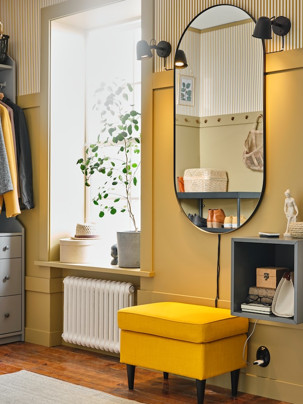 A LINDBYN mirror is mounted on a wall above a STRANDMON footstool and a dark grey EKET wall-mounted shelving unit.