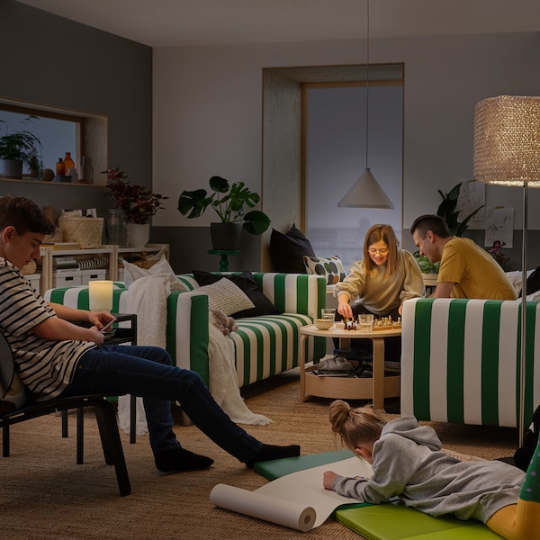 A living room centred around two green-and-white-striped sofas, where a family is engaged in drawing and playing chess.