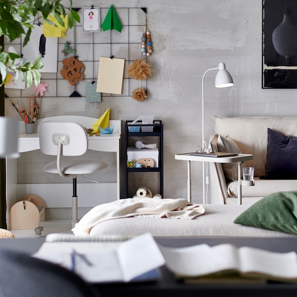 A neutral-toned living room with a white desk and work chair in the corner. A memo board is on the wall above.