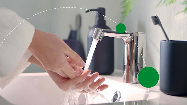 A pair of hands under a running bath faucet, with green graphic dots to imply sustainability.