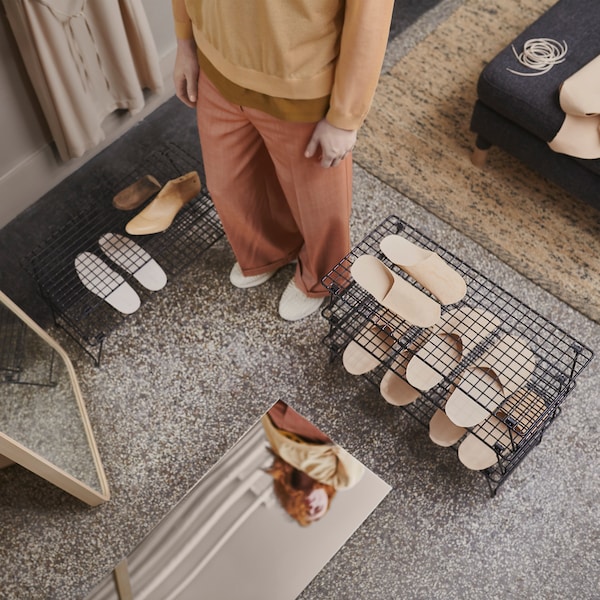 A person stands in a hallway where there are two mirrors and a lot of shoes placed on stackable GREJIG shoe racks.