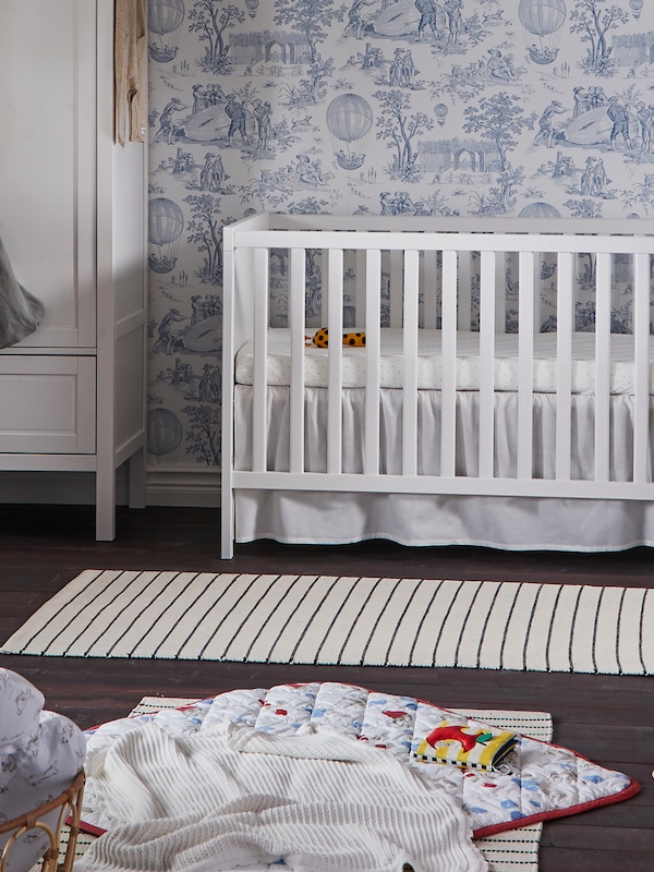 A SUNDVIK crib stands near a SUNDVIK wardrobe in a traditional children’s room with blue and white wallpaper.