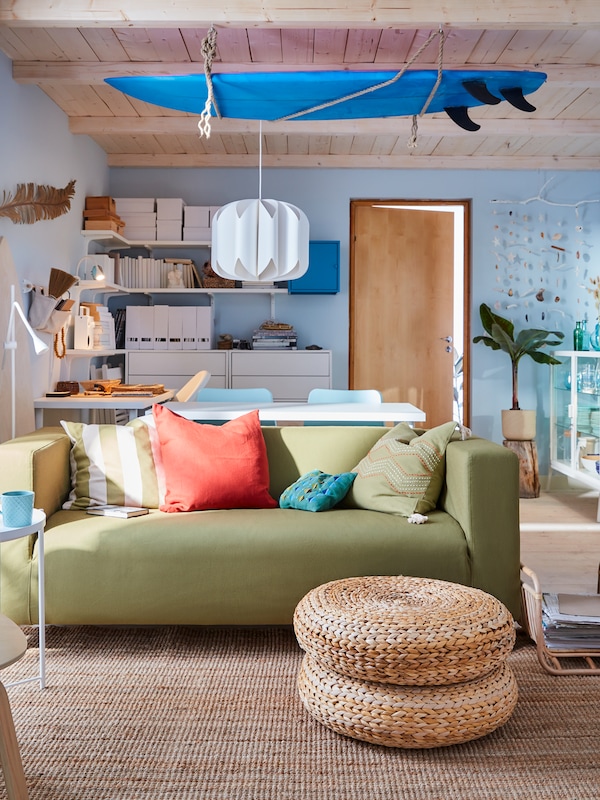 A surf-inspired living room with a yellow-green sofa, blue surfboard on the ceiling, white shelves, and blue walls.