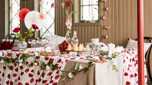 A table set for a party with many items from the ANLEDNING collection including a white/red tablecloth and glasses.