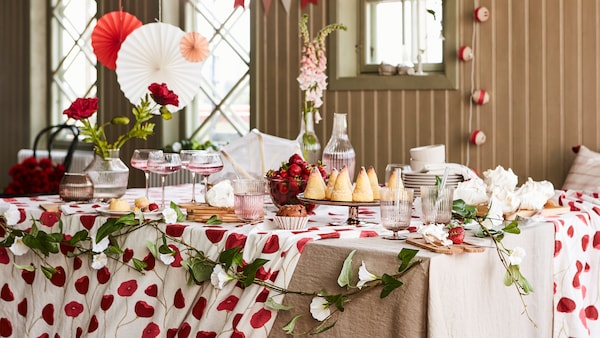 A table set for a party with nice glasses, sweet things things to eat, flowers and festive hanging decorations in red/white.