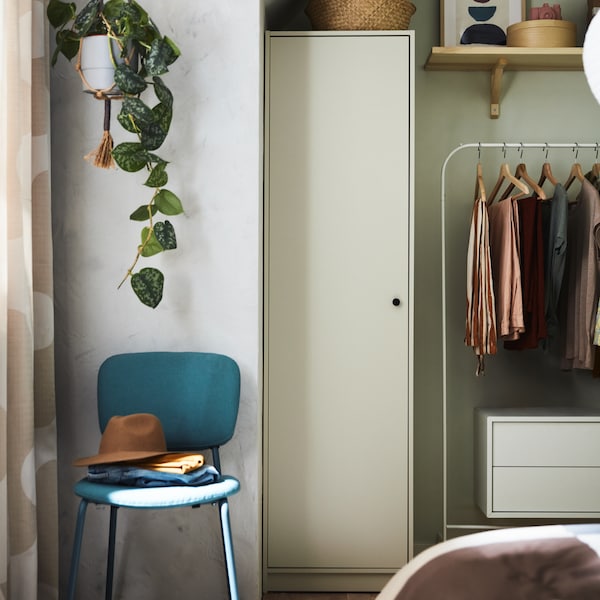 A turquoise KARLJAN chair stands in a corner of a bedroom underneath a plant in a hanging pot and near a GURSKEN wardrobe.