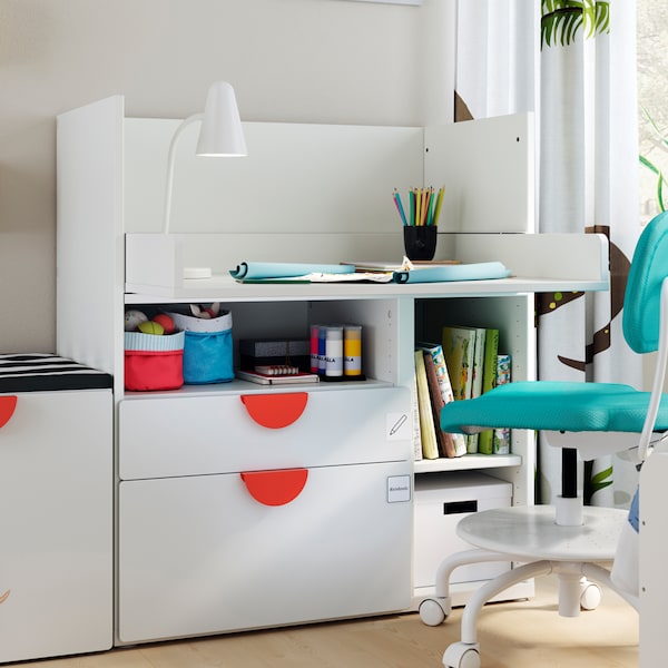 A VIMUND children’s desk chair sits at a white SMÅSTAD desk with 2 drawers. There is a FUBBLA LED work lamp on the desk.