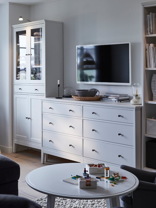 A white and grey tone living room with an IDANÄS glass door cabinet, chest of drawers and bookcase in a line along the wall.