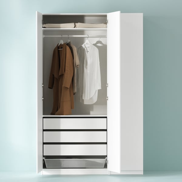 A white PAX wardrobe stands partly open. There are clothes hanging from a rail, drawers, shelves and a basket inside.