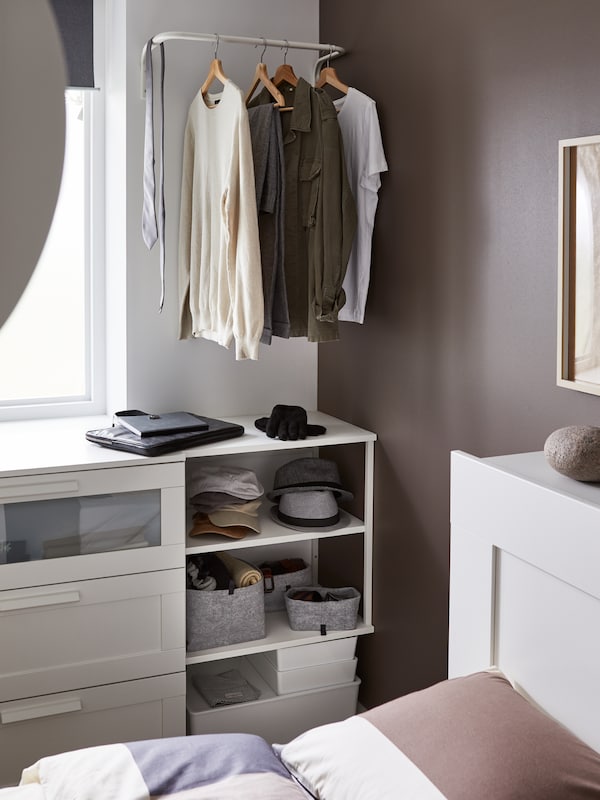 A white rail above open shelves with sweaters, t-shirts and a necktie hanging on it. Hats are on the shelves.