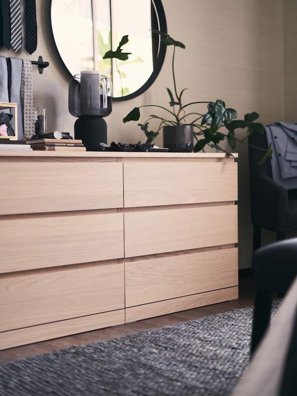 A white-stained oak veneer MALM chest of six drawers with a speaker lamp on top, and a grey rug in front of it.