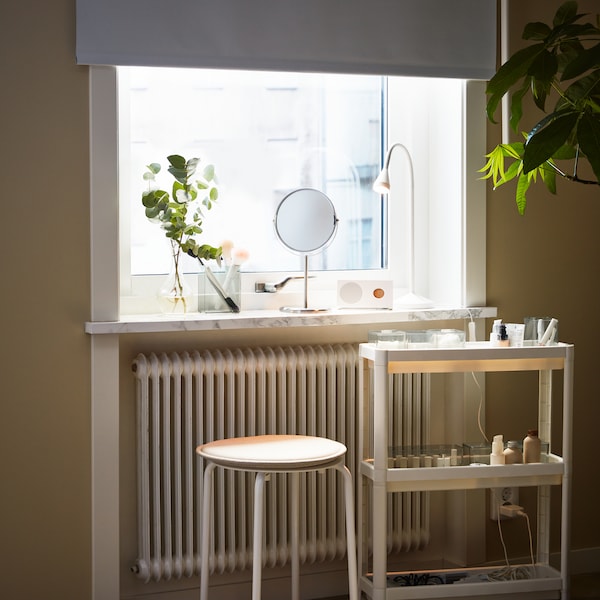 A white VESKEN trolley and a white MARIUS stool stand in front of a window with different objects on the windowsill.