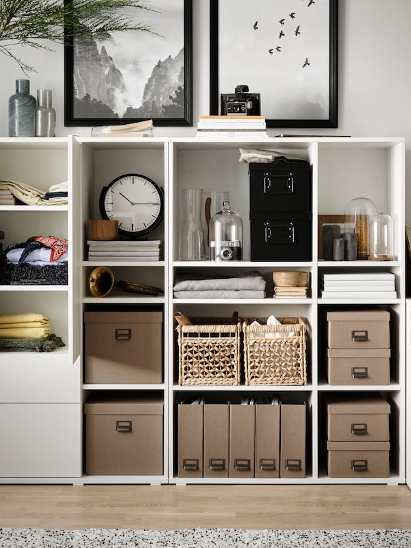 A white VIHALS storage unit with neatly arranged boxes and baskets, a clock, magazines, and two framed artworks above it.