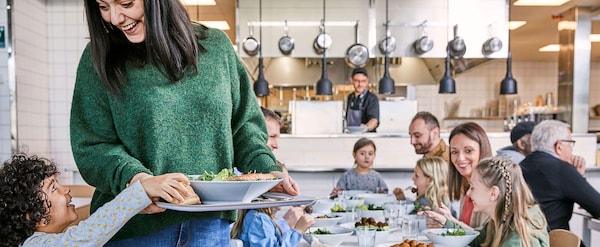 A woman in a green sweater holding a tray of food with people