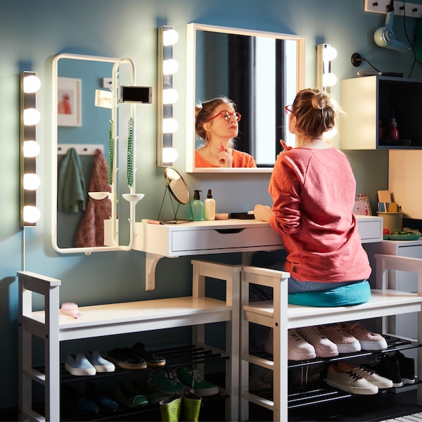 A woman sits on a cushion on a HEMNES bench with shoe storage and does her make-up in front of a NISSEDAL mirror.