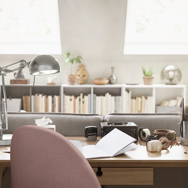 A workspace at home with a work lamp and a swivel chair and a LISABO desk in ash veneer behind a sofa.