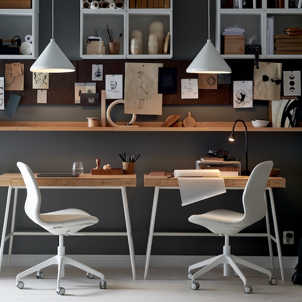 A workspace where two LÅNGFJÄLL office chairs sit at LILLÅSEN desks, with shelving, memo boards and white pendant lamps.