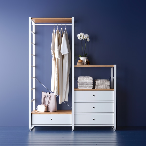 An ELVARLI wardrobe combination stands in a blue room holding clothes hanging on a rail, bags and other items.