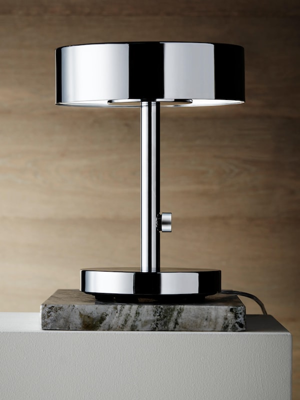 Contemporary decor style table lamp with sleek metal on stone base atop table. 