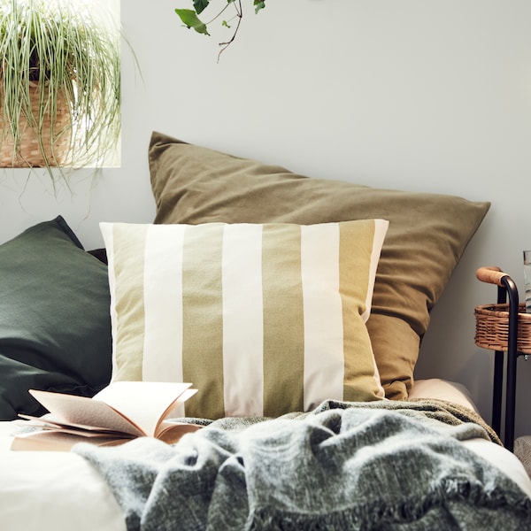 Cushions in different cushion covers including one in a striped HILDAMARIA cushion cover sit on a bed near a window.