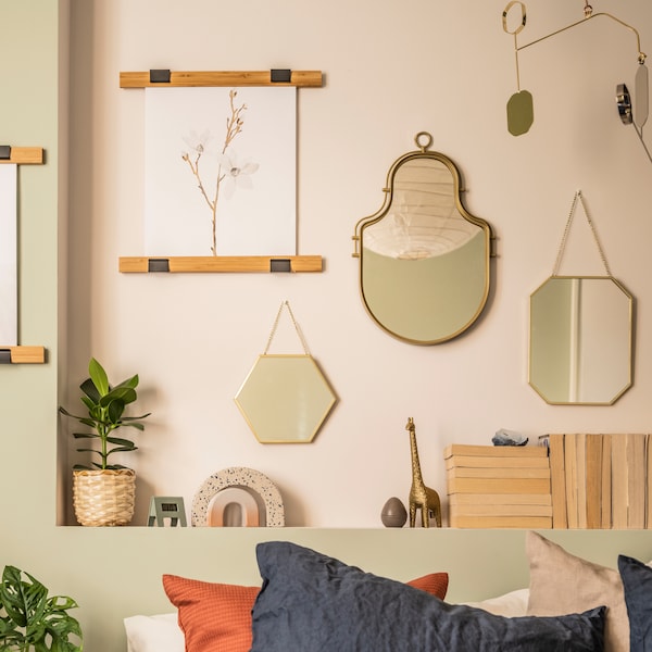 Gold-colored LASSBYN mirrors in various sizes hang on a pink wall with a green ledge below where decorative objects stand.