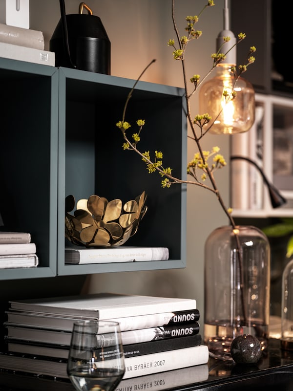 Grey-turquoise EKET wall-mounted shelving units on a living room wall, books and decorations in and around them.