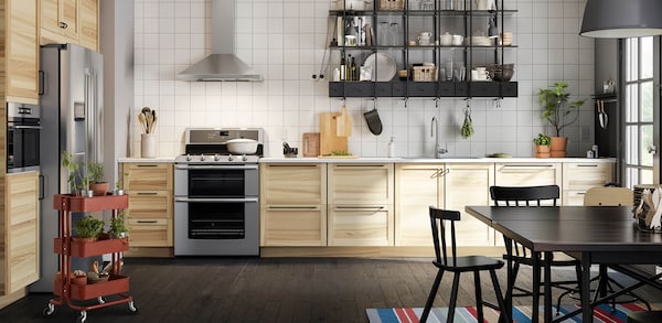 Image of a kitchen with wooden door fronts and stainless teel appliances with a dark kitchen table and chair set.