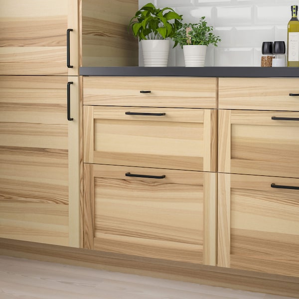 Kitchen cabinets in a natural wood color with a dark countertop and green plants on the counter.