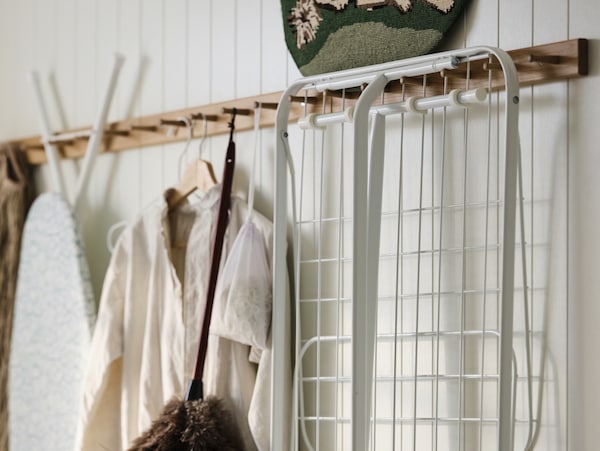 Laundry, cleaning and ironing accessories hanging on a white, wood-panelled wall.