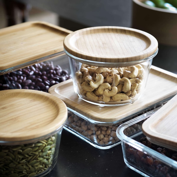 Nuts and dried beans in glass storage containers with wooden lids on kitchen counter. 