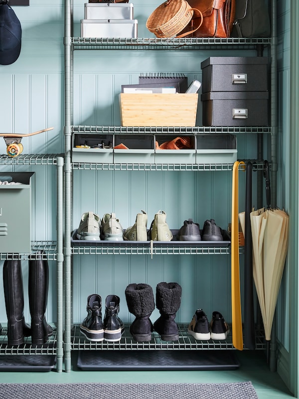 OMAR shelving holding boxes, bags, footwear and other items stands in a corner of a hallway.