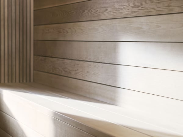 Pale wooden boards forming a bench seat inside a sauna with sunlight falling across the seating.