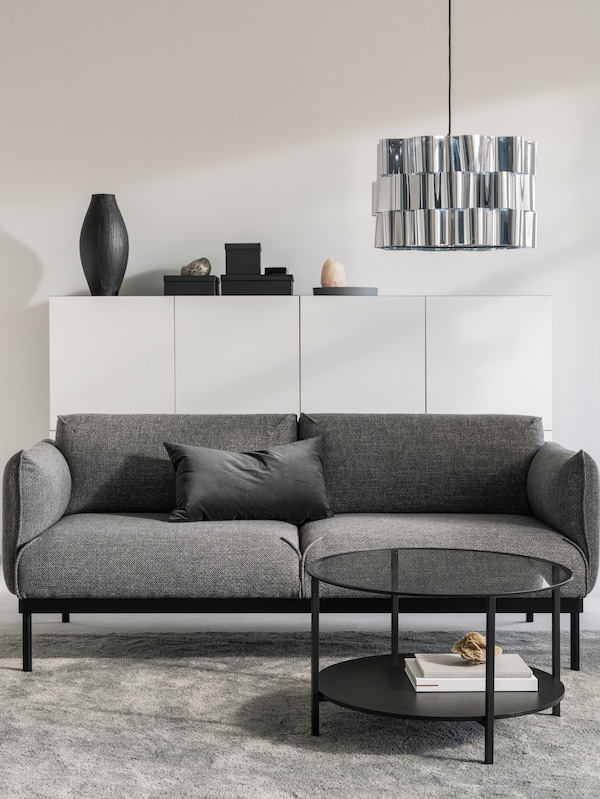 A living room with white walls, a grey/black ÄPPLARYD sofa, a coffee table and white storage units.